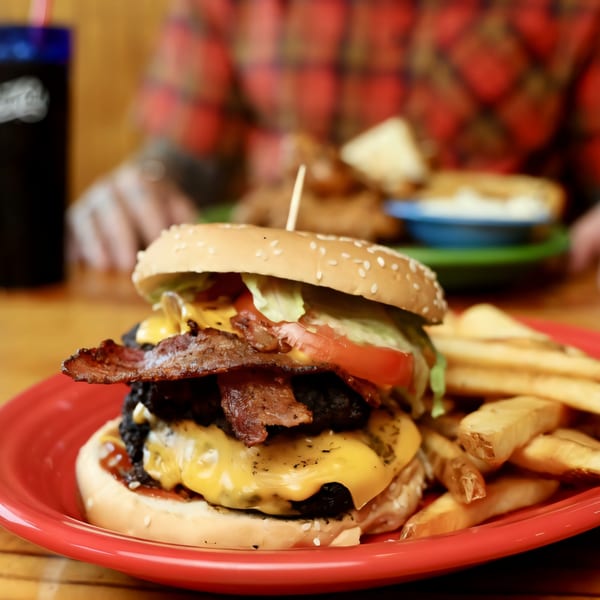 A Big B Barbecue double cheeseburger with bacon, lettuce, tomato, and fries on a red plate.
