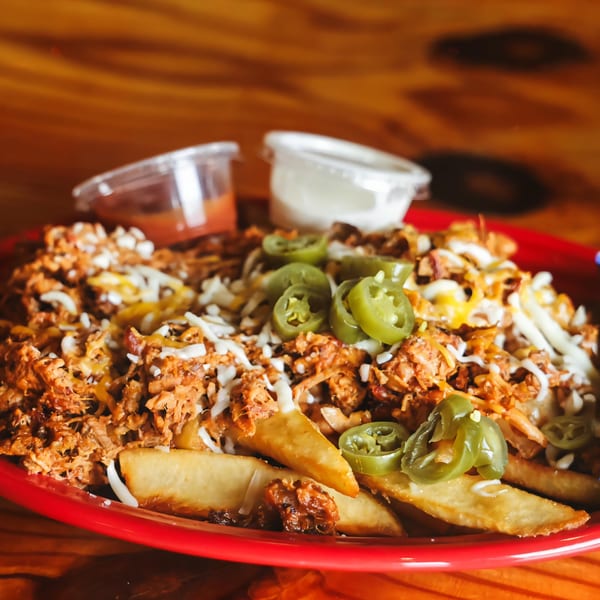 Big B Barbecue's loaded fries with pulled pork, cheese, jalapeños, and sauces on a red plate.
