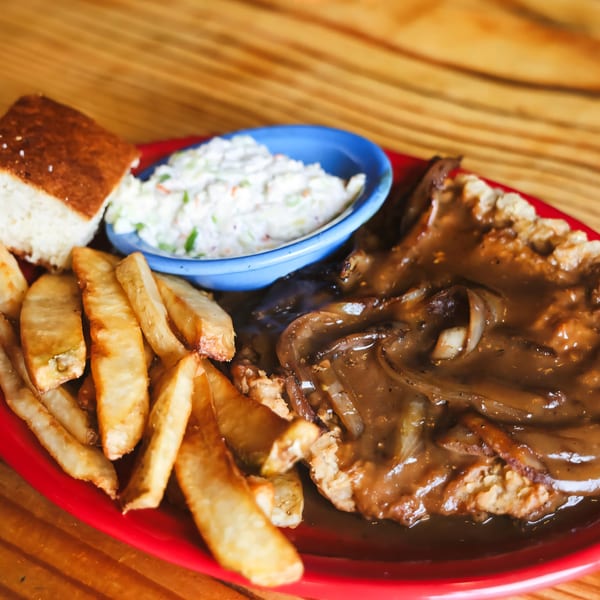 Big B Barbecue's country fried steak with gravy, fries, coleslaw, and cornbread on a red plate.