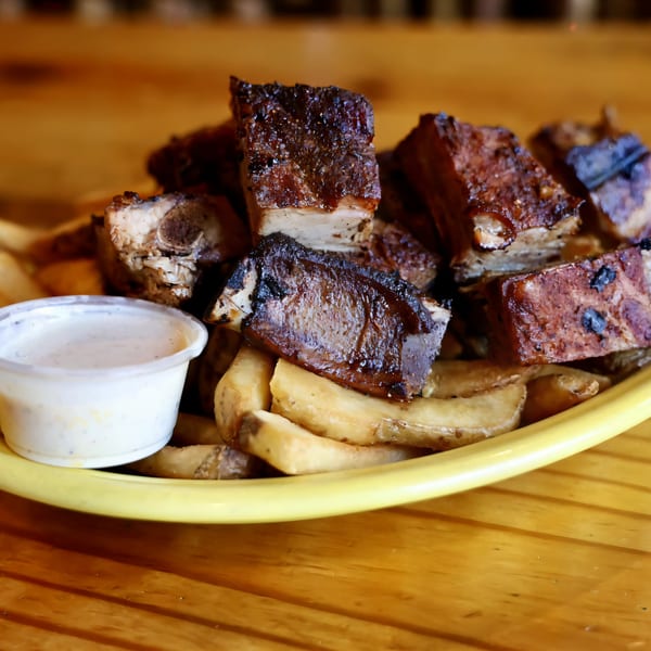 Big B Barbecue's grilled ribs and fries with a side of dipping sauce on a yellow plate.